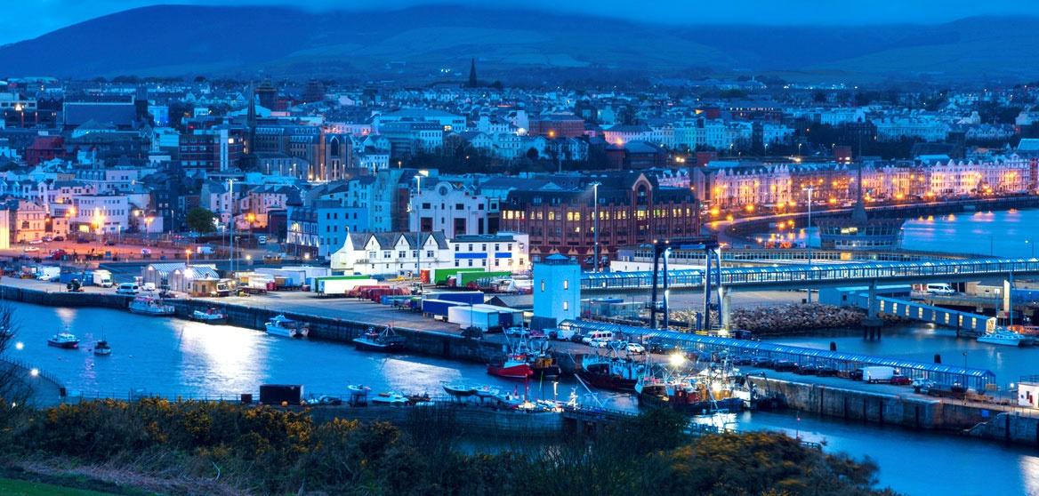 Scenic evening view of the Isle of Man coastline, featuring rugged cliffs, and clear blue water.