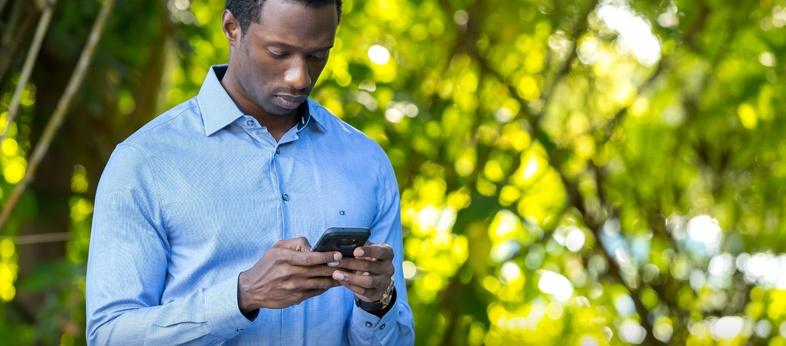 Man focussed on his smartphone wearing a blue long sleeve shirt. 