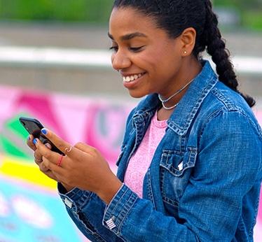 Young woman smiling at her smartphone wearing a pink short with a denim jacket.